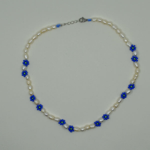 Eine handgefertigte Perlenkette mit Gänseblümchen-Motiven, gemeinsam mit einer türkischen Kunsthandwerkerin hergestellt. Die Perlen sind naturbelassen und variieren in Form, Größe und Farbe. Die Kette wird in einem kleinen Stoffbeutel zur AufbewahrEine handgefertigte Perlenkette mit Gänseblümchen-Motiven, gemeinsam mit einer türkischen Kunsthandwerkerin hergestellt. Die Perlen sind naturbelassen und variung geliefert. Der Ton ist elegant und herzlich und betont Handwerkskunst sowie kulturelle Authentizität.