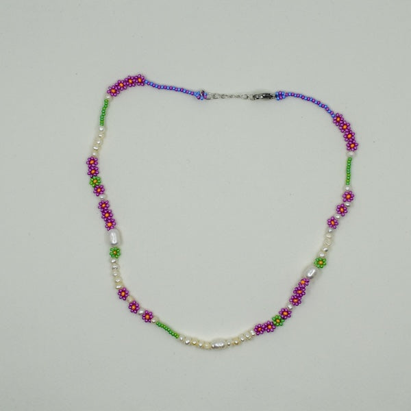 Eine handgefertigte Perlenkette mit Gänseblümchen-Motiven, gemeinsam mit einer türkischen Kunsthandwerkerin hergestellt. Die Perlen sind naturbelassen und variieren in Form, Größe und Farbe. Die Kette wird in einem kleinen Stoffbeutel zur Aufbewahrung geliefert. Der Ton ist elegant und herzlich und betont Handwerkskunst sowie kulturelle Authentizität.
