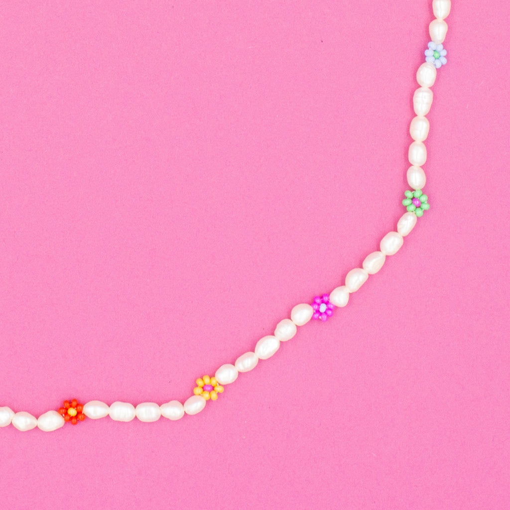 A handcrafted pearl necklace featuring daisy motifs, made in collaboration with a female artisan from Turkey. The pearls are natural and unique in shape, size, and color. The necklace is presented with a small fabric sack for safe keeping. The tone is elegant and warm, highlighting craftsmanship and cultural authenticity.